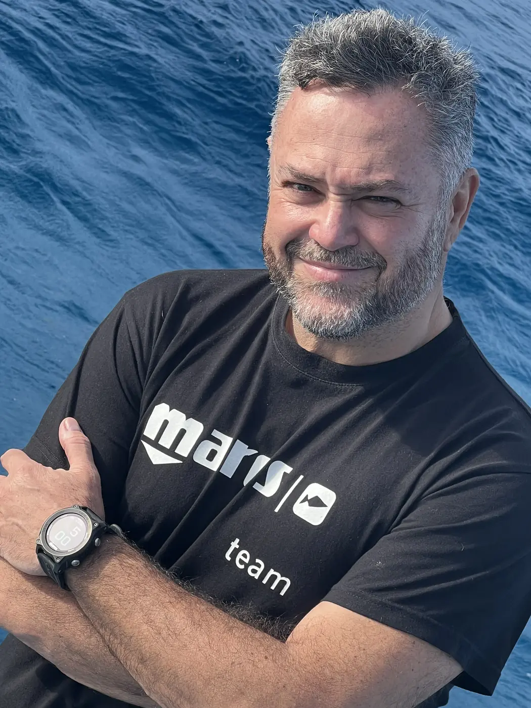 Retrato de Karlos Simón con los brazos cruzados, sonriendo frente al mar